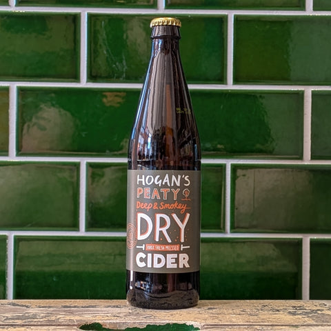 Bottle of Hogan's Peaty Dry Cider against a green tiled wall.